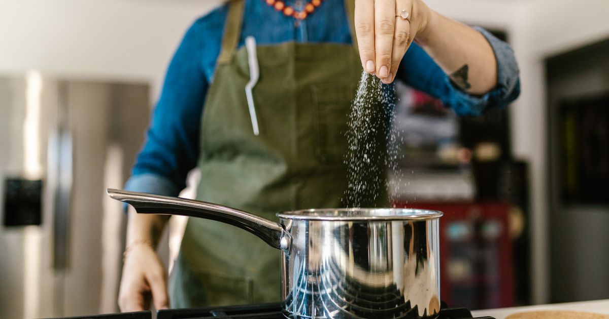 A woman adding iodized salt to a pot on the stove while cooking
